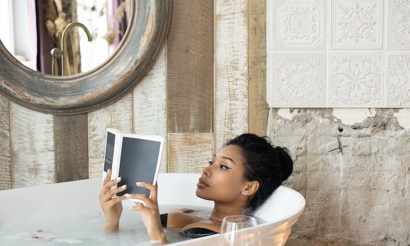 Young black woman reading book in bath